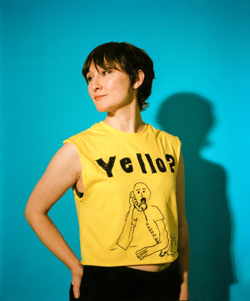 headshot of Stark Holborn wearing a yellow t shirt that says Yello against a blue background